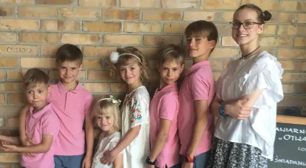Szczęśliwa rodzina wielodzietna pozuje do zdjęcia na tle ceglanej ściany.