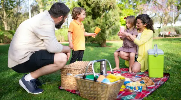 Radosny piknik rodzinny w parku. Rodzice i dzieci cieszą się wspólnym czasem na kocu, wśród zieleni.