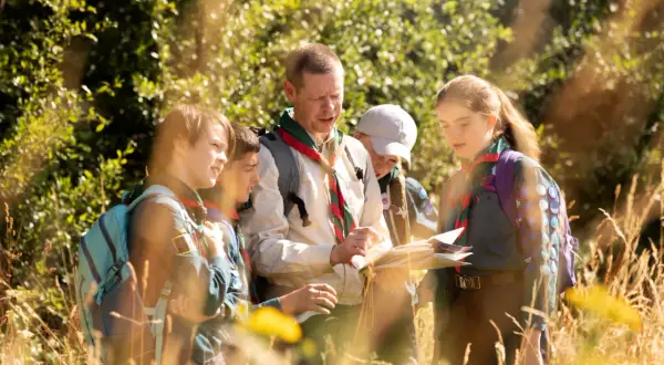 Grupa harcerzy z kierownikiem obozu, który jest też wychowawcą, analizuje mapę w lesie.