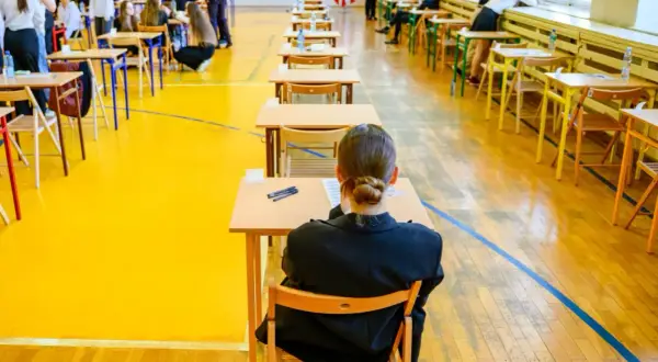 Uczniowie siedzą przy ławkach w sali gimnastycznej, przygotowując się do egzaminu dojrzałości.