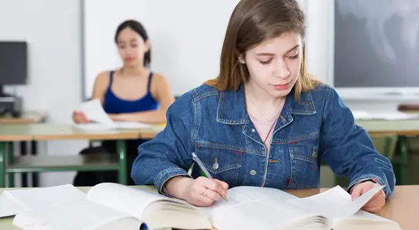 Dziewczyna w dżinsowej kurtce pisze notatki, przygotowując się do egzaminu poprawkowego.