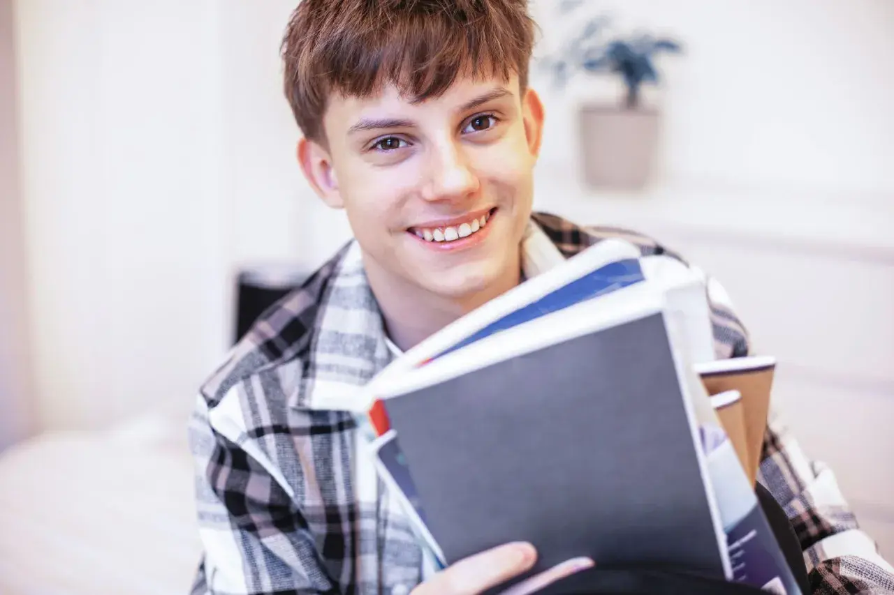 Uśmiechnięty student z książkami, zastanawia się, jak rozliczyć dochody dziecka pełnoletniego uczącego się.