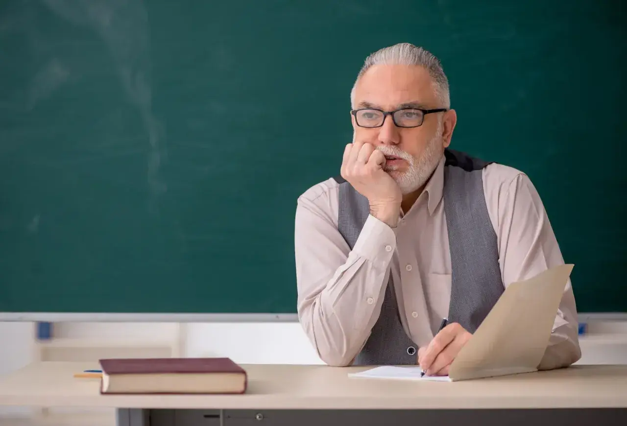 Starszy nauczyciel zamyślony nad dokumentami, być może planuje swoją sześciomiesięczną odprawę emerytalną.