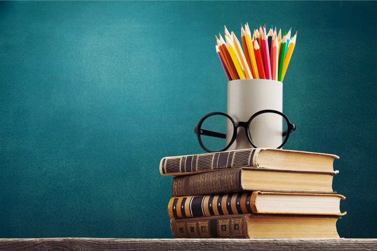Stos książek, okulary i kolorowe kredki symbolizują drogę do wiedzy, która zaczyna się od wykształcenia średniego.