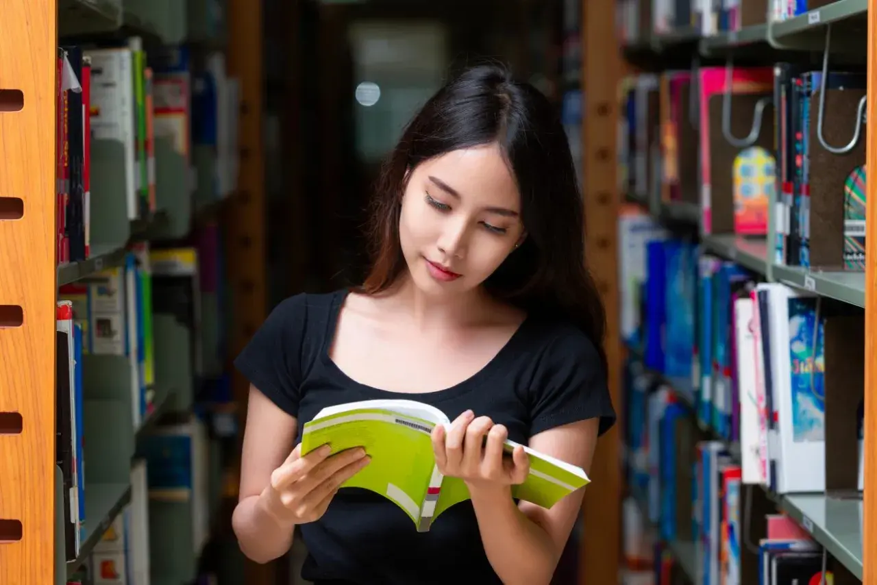 Młoda kobieta w bibliotece, pochłonięta lekturą. Czy jej oceny pozwolą jej uzyskać stypendium?
