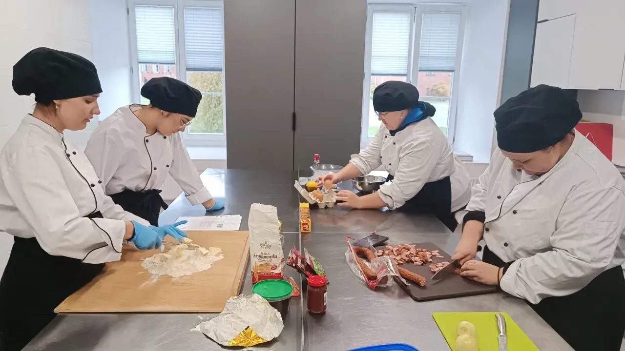 Uczniowie na kierunku technik żywienia i usług gastronomicznych ćwiczą krojenie kiełbasy i przygotowanie ciasta.