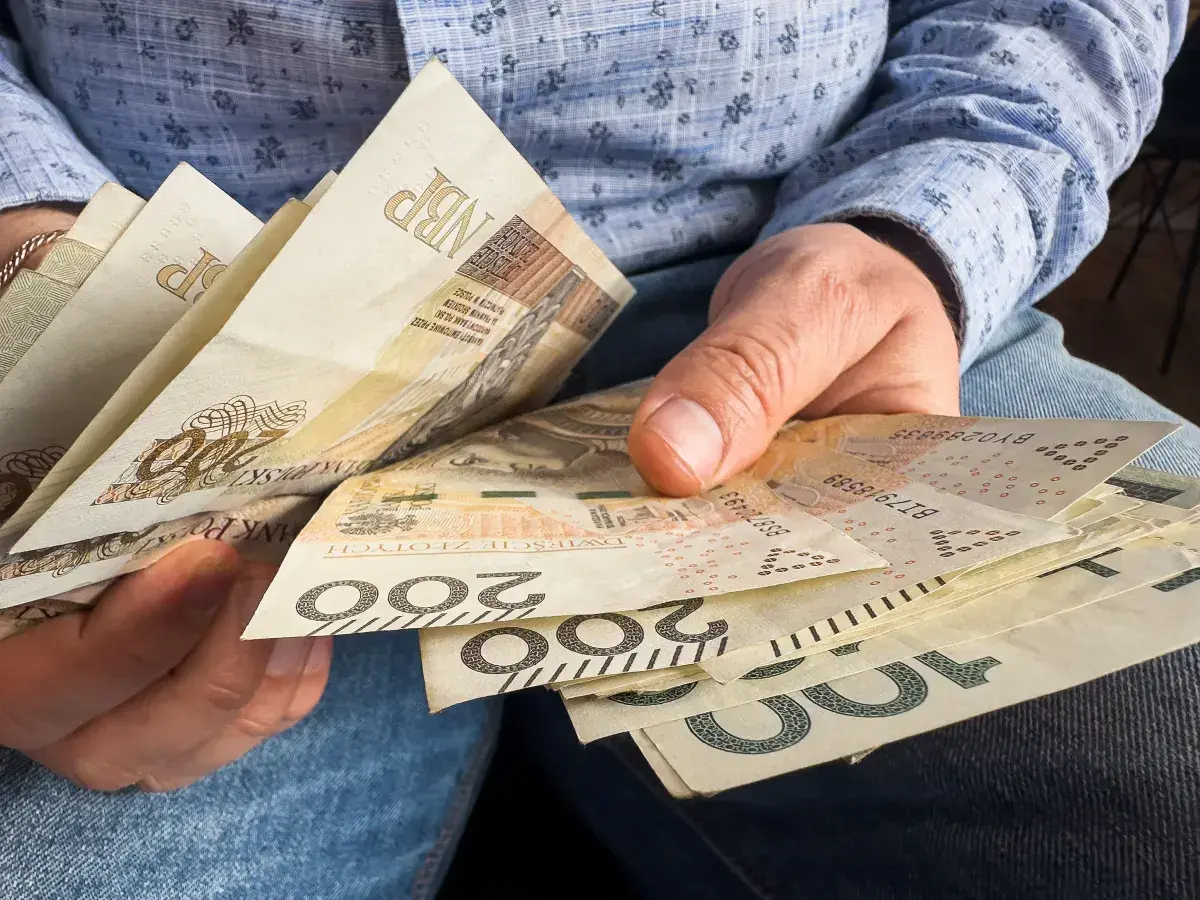 Dłonie trzymają polskie banknoty 200 zł i 100 zł. Zastanawiasz się, czy 800 plus wlicza się do dochodu?