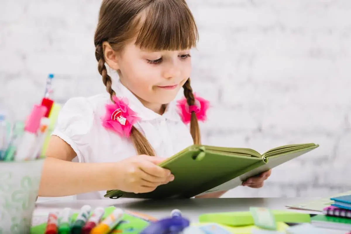 Dziewczynka z warkoczami czyta książkę, marząc o przyszłości, gdy zdobędzie kurs pedagogiczny uprawniający do pracy w szkole.