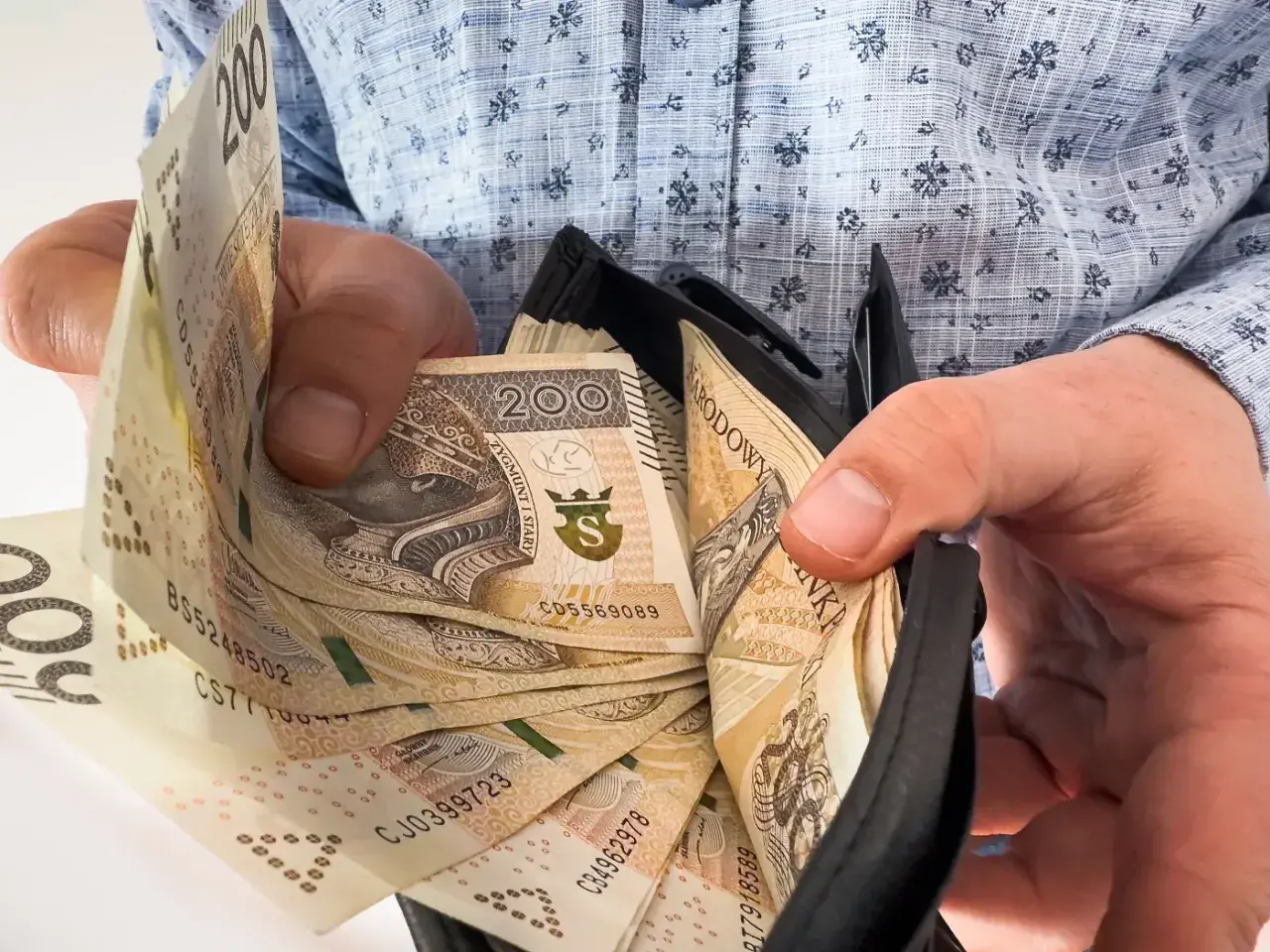 Ręce trzymają portfel z banknotami 200 zł. To nagroda jubileuszowa za 15 lat pracy, symbol docenienia za lata zaangażowania.