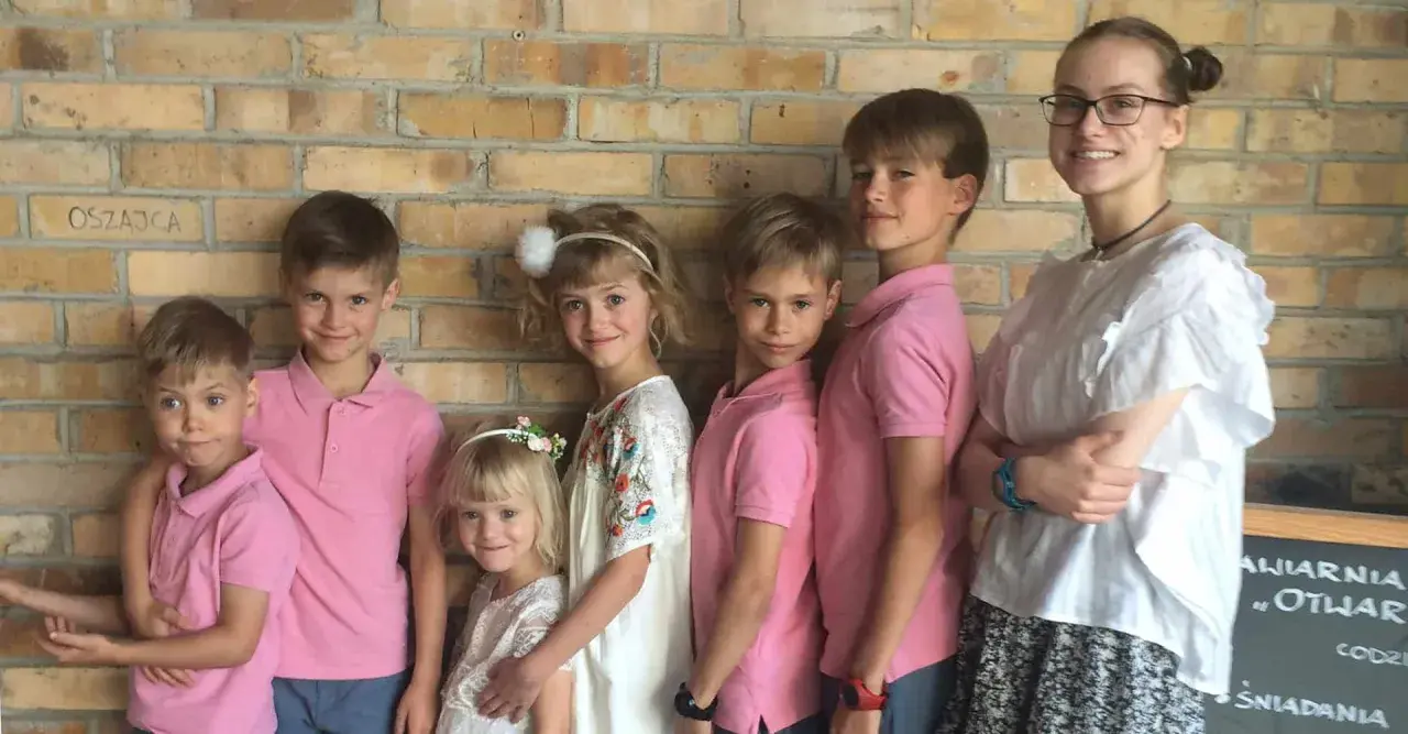 Szczęśliwa rodzina wielodzietna pozuje do zdjęcia na tle ceglanej ściany.