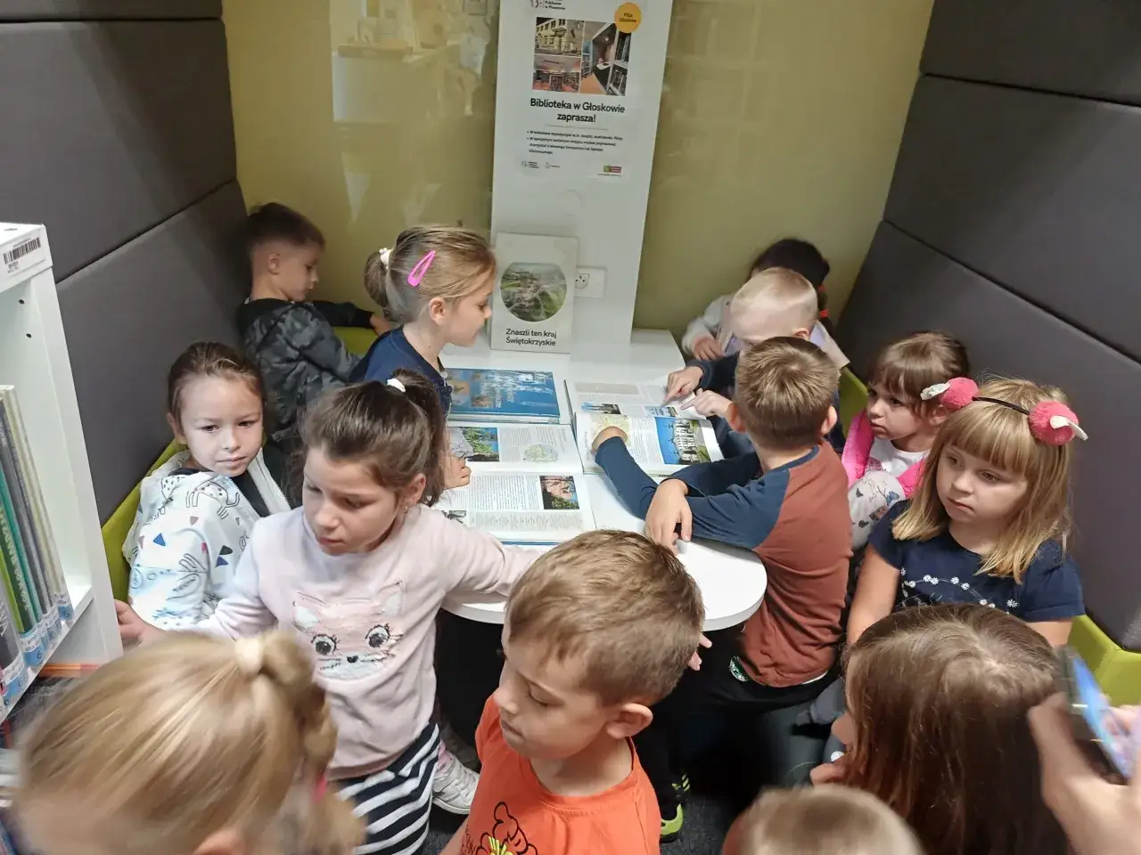 Dzieci słuchają opowieści bibliotekarza w przytulnej czytelni.