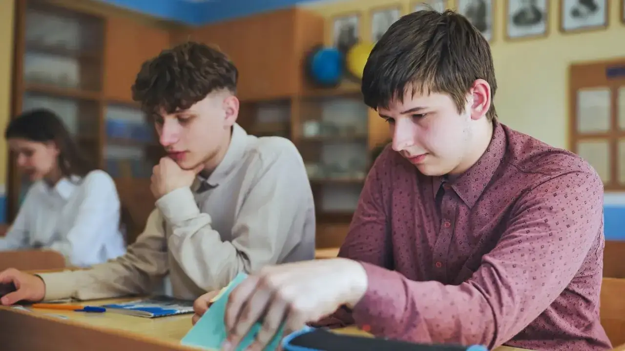 Uczeń zamyślony nad zeszytem, być może szuka usprawiedliwienie nieobecności w szkole.