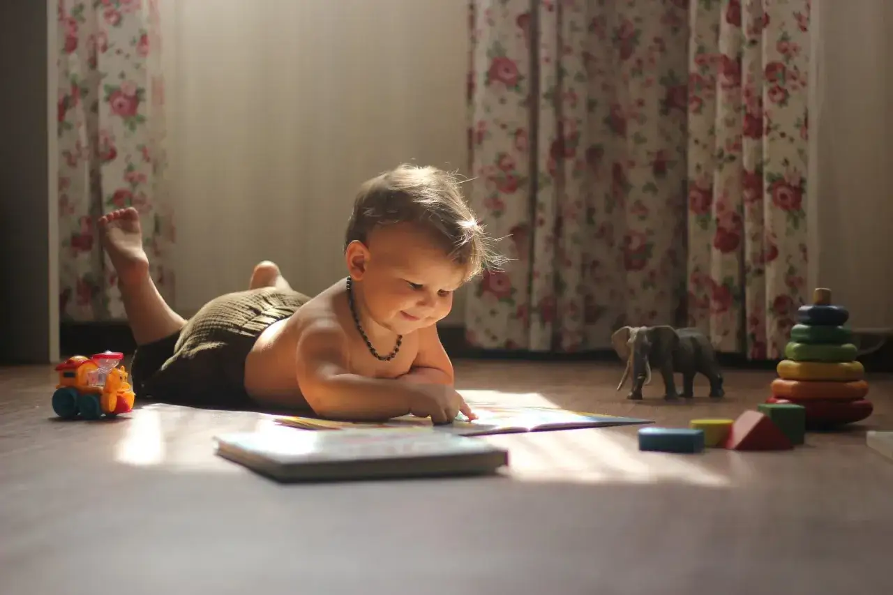 niemowlę na macie edukacyjnej unosi główkę i sięga po zabawkę