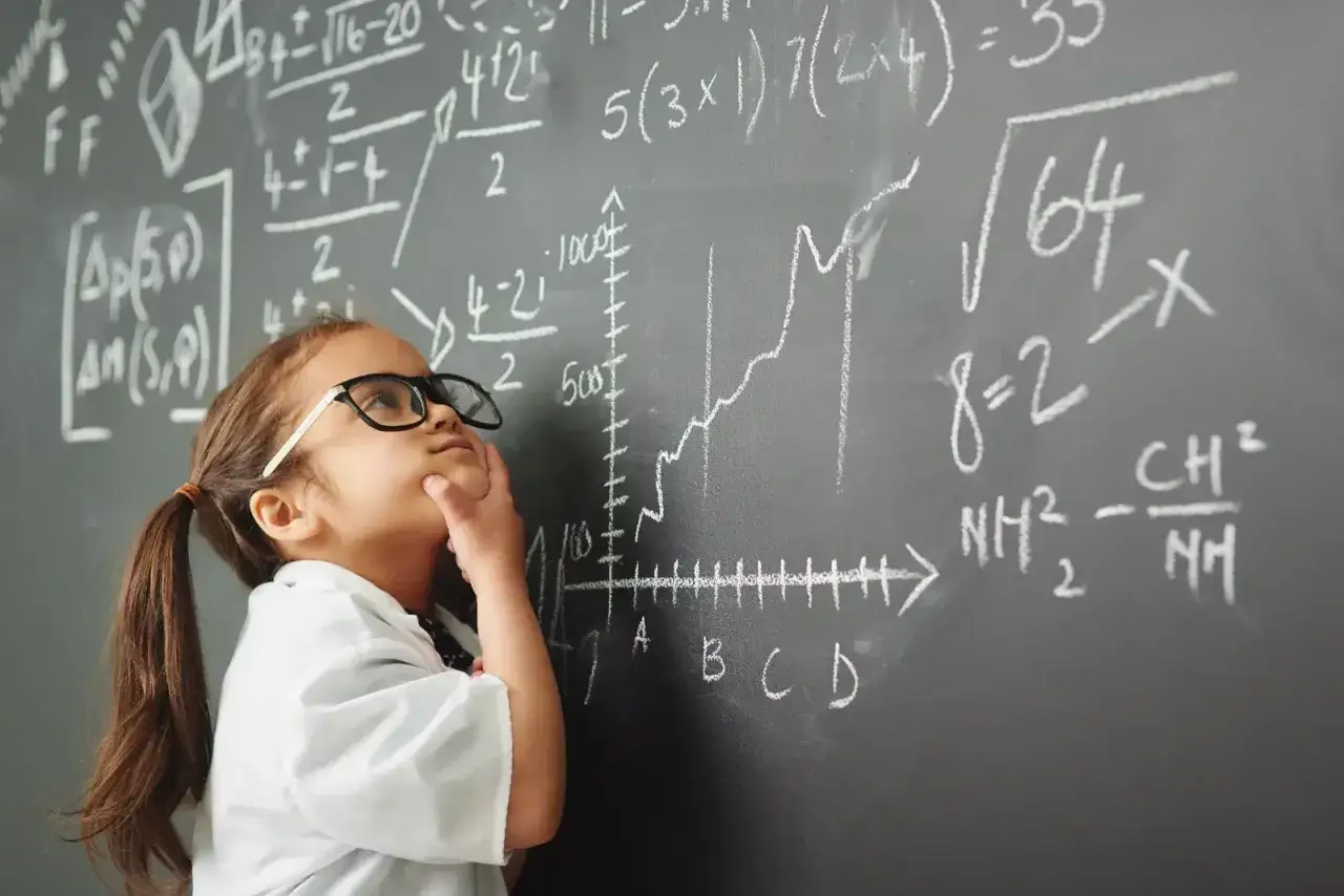 Dziewczynka w okularach zamyślona nad skomplikowanymi równaniami na tablicy. Nawet z dyskalkulią, próbuje zrozumieć matematykę.