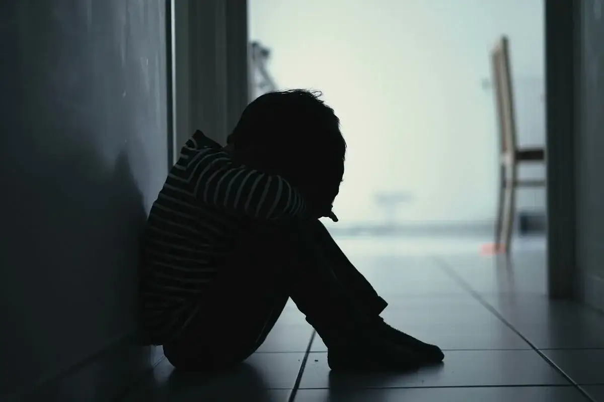 Dziecko skulone w kącie, przeżywające skutki bullyingu w szkole. Ciemna sylwetka na tle jasnego korytarza.