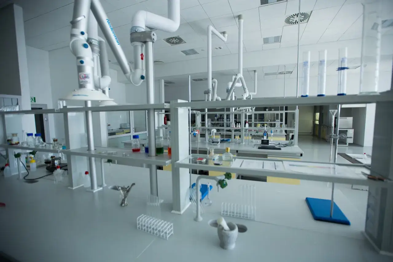 Nowoczesne laboratorium, gdzie technik analityk przeprowadza badania. Widać stoły laboratoryjne, sprzęt, probówki i kolby.