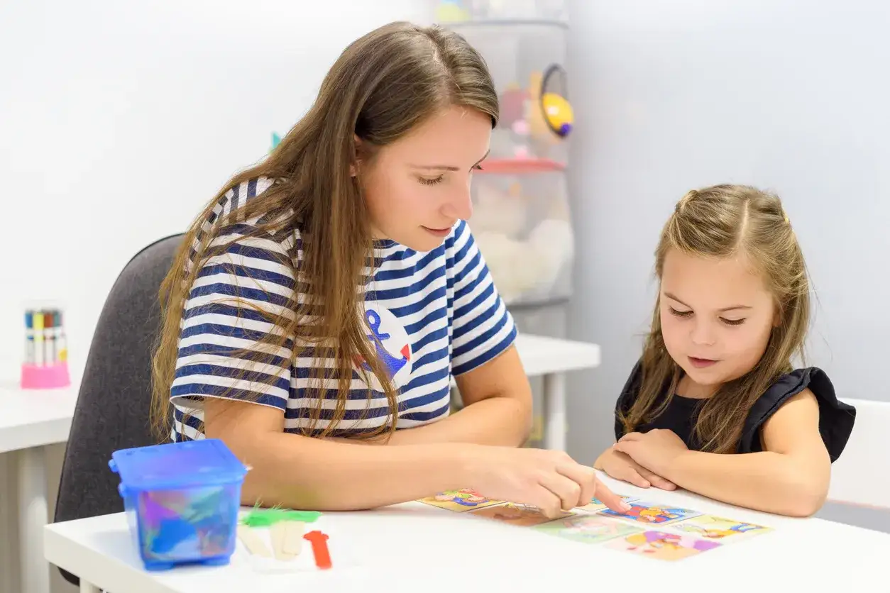 Nauczycielka z kursem pedagogicznym uprawniającym do pracy w szkole, z zaangażowaniem tłumaczy dziecku obrazki z gry edukacyjnej.