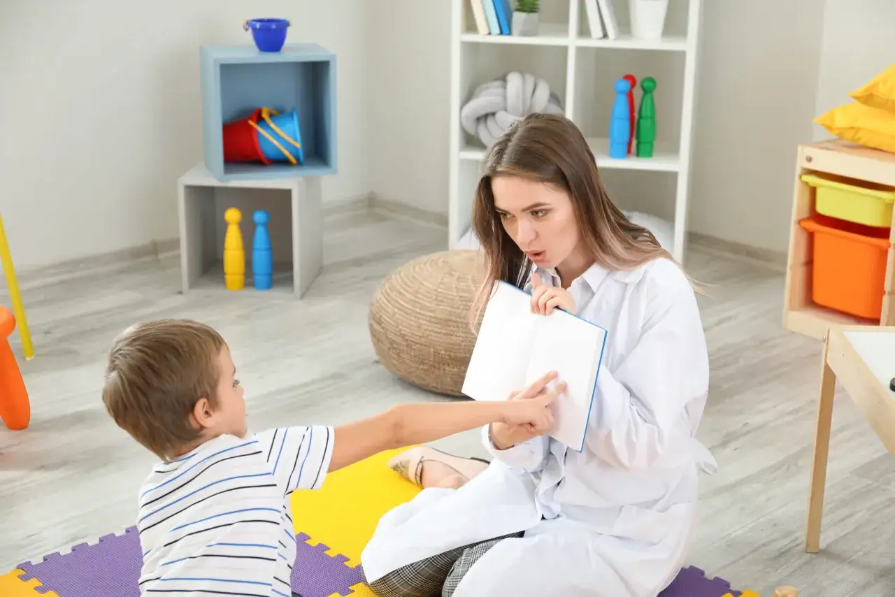 Terapeuta pracuje z dzieckiem, pomagając mu w terapii afazji. Pokazuje mu książkę, ćwicząc mowę i komunikację.