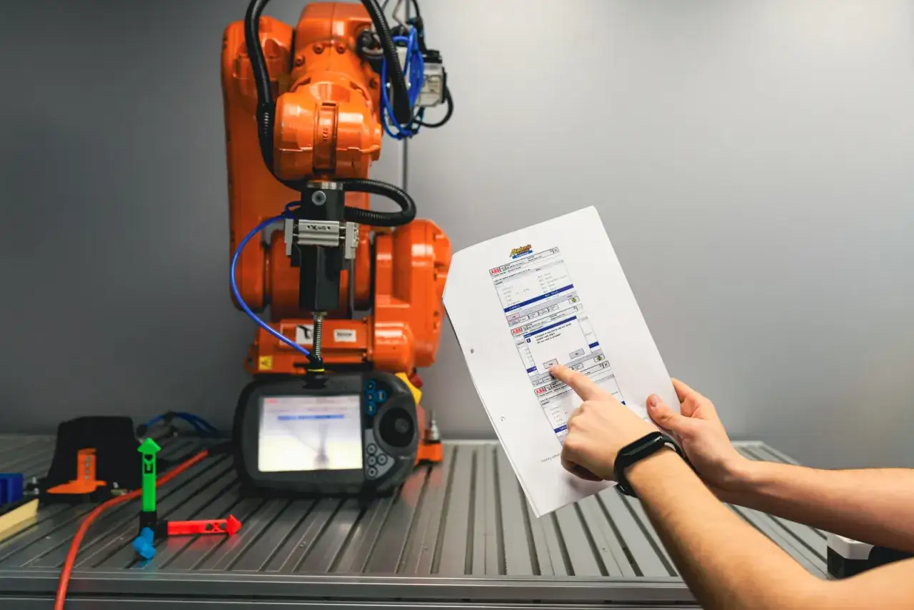 Technik robotyk sprawdza dokumentację przy pomarańczowym robocie przemysłowym.