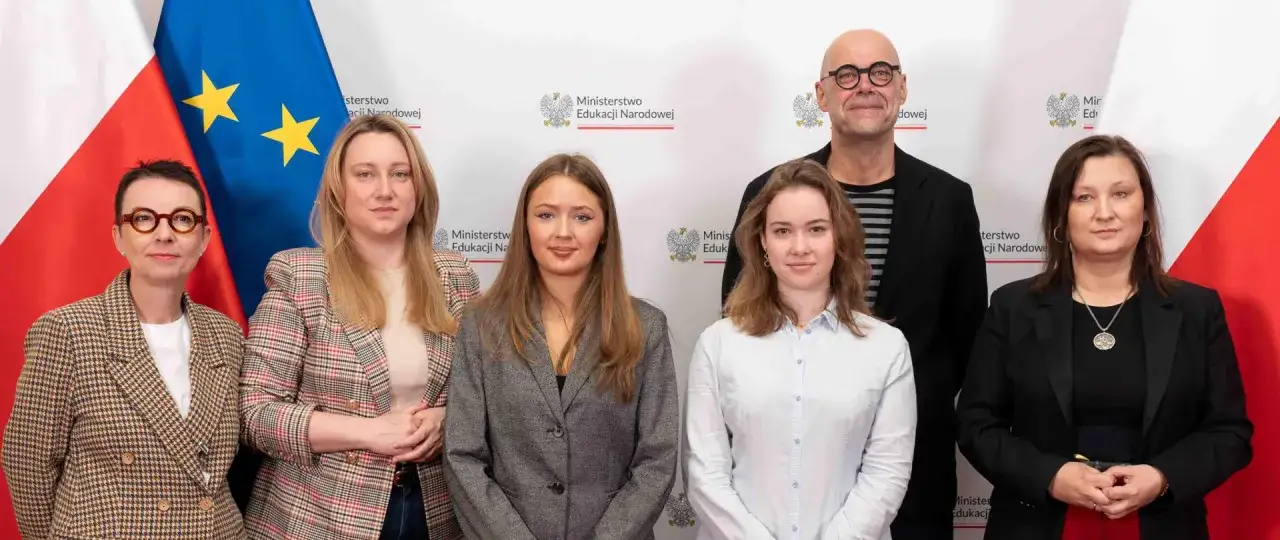 Wiceminister edukacji z zespołem na tle flag Polski i UE.