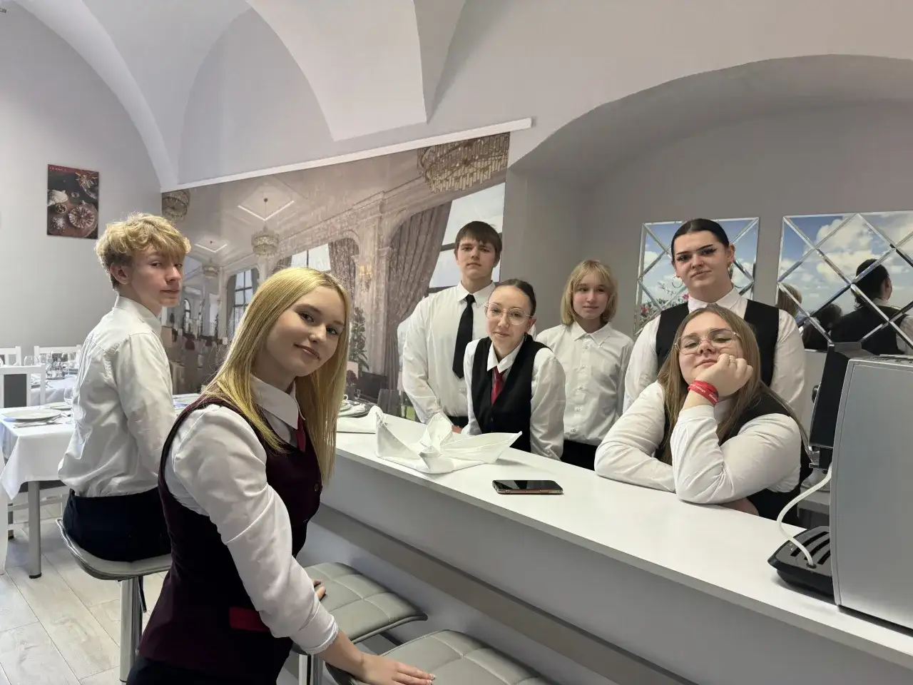 Grupa młodych ludzi w strojach kelnerskich, przyszli technicy hotelarstwa, pozuje do zdjęcia przy barze.