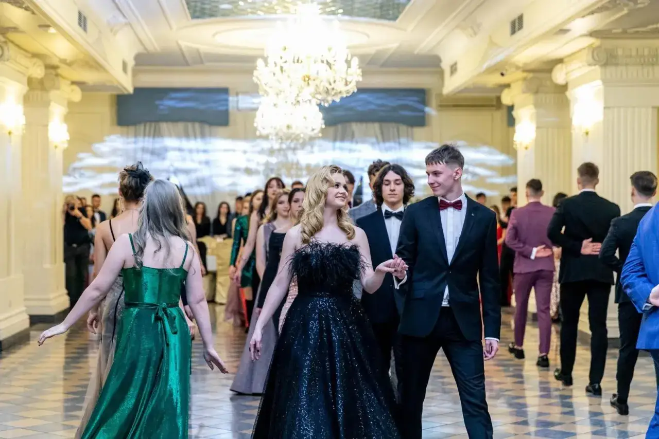 Młoda para w eleganckich strojach, ona w czarnej sukni, on w garniturze, idzie na bal studniówkowy.