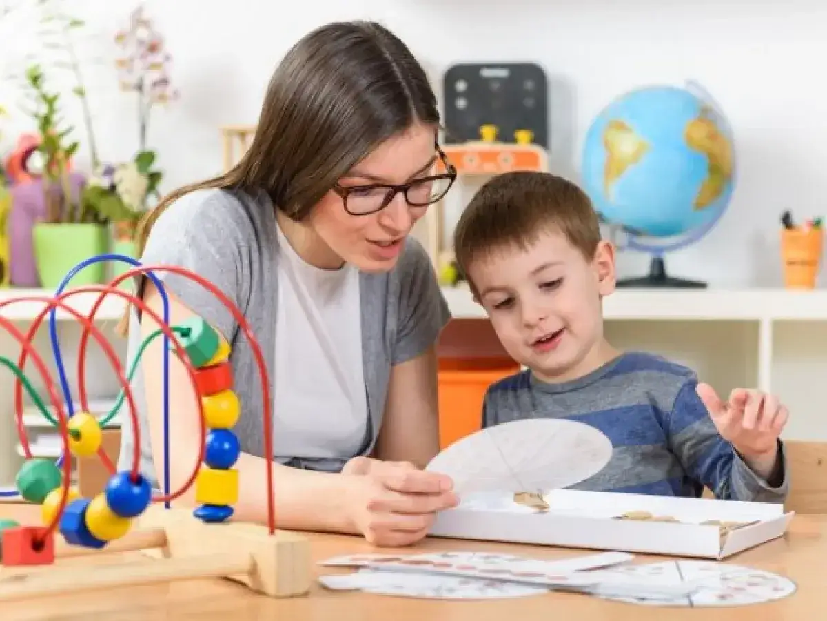 Nauczycielka z okularami wspiera chłopca w zabawie edukacyjnej. Pomoc psychologiczno pedagogiczna w praktyce.