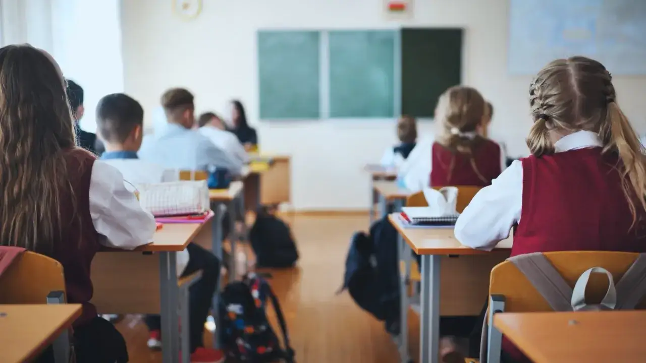 Dzieci siedzą w ławkach, słuchając lekcji. Nowy przedmiot w szkole budzi ciekawość.