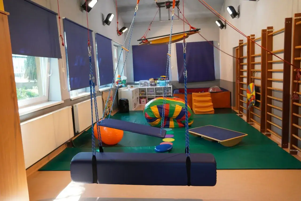 Sala do zajęć rewalidacyjno-wychowawczych z huśtawkami, drabinkami i kolorowymi materacami.