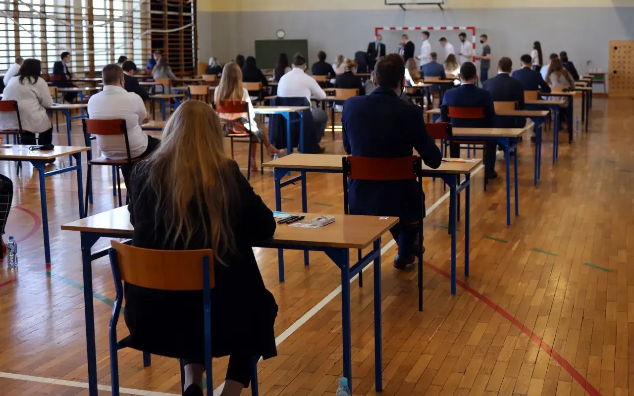 Uczniowie siedzą w ławkach, skupieni na zadaniach. Atmosfera napięcia i ciszy towarzyszy im podczas egzaminu dojrzałości.