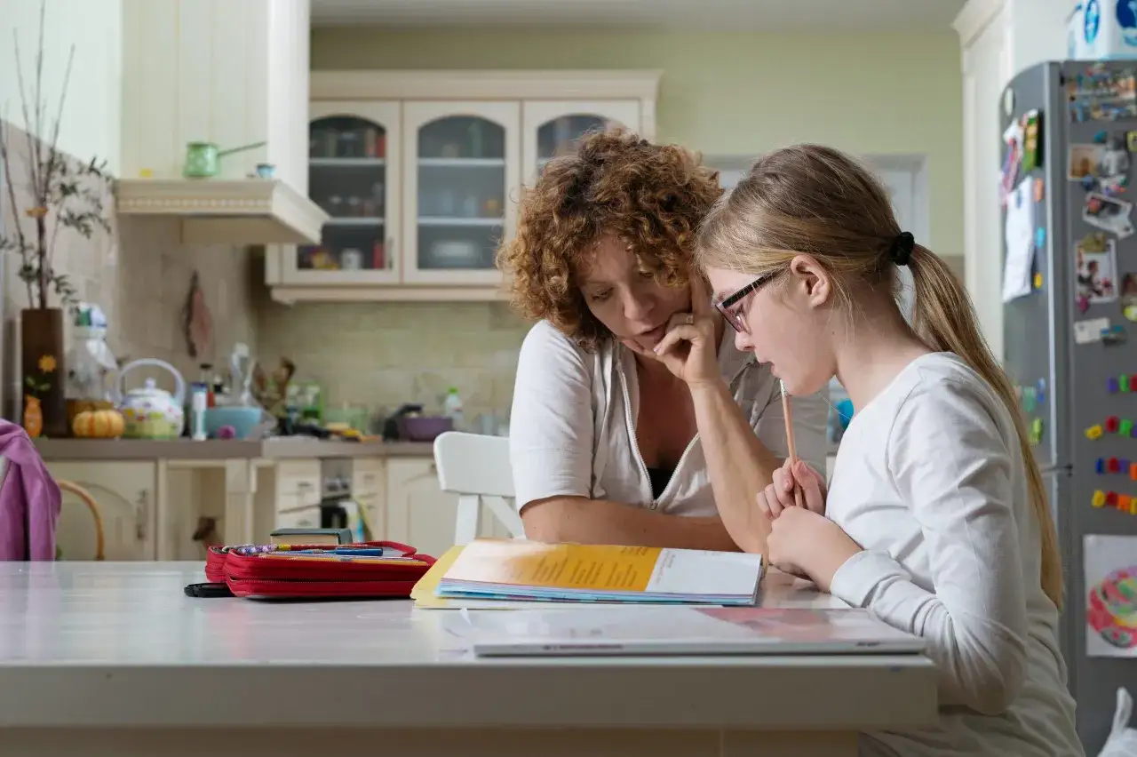 Mama cierpliwie tłumaczy zadanie córce, która ma dysleksję. Dziewczynka z uwagą słucha, trzymając ołówek.