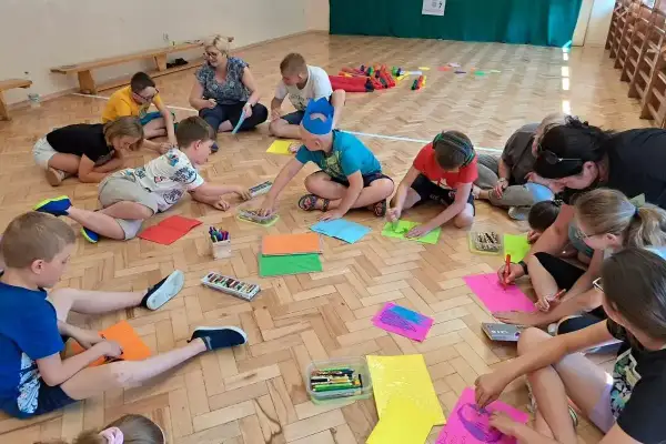 Dzieci klas 1-3 biorą udział w zabawach integracyjnych, rysując na kolorowych kartkach.