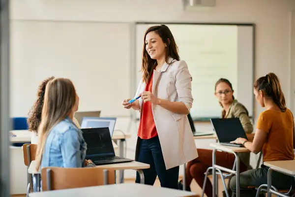 Nauczycielka wita studentów, omawiając jak zostać nauczycielem. W sali lekcyjnej panuje atmosfera nauki i zaangażowania.