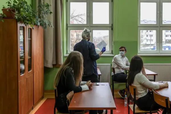 Nauczyciel dyplomowany zarobki - lekcja w klasie, uczniowie siedzą przy ławkach, nauczyciel stoi przy oknie z dokumentami.