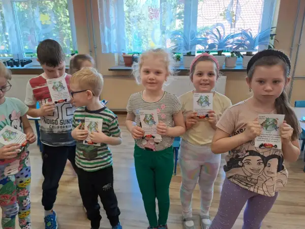 Dzieci z oddziału przedszkolnego świętują Dzień Ziemi, trzymając w rękach kartki z motywem planety i słodkości.