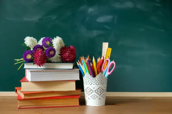 Kwiaty na stosie książek i przybory szkolne na tle zielonej tablicy. Idealna kompozycja na Dzień Edukacji Narodowej.