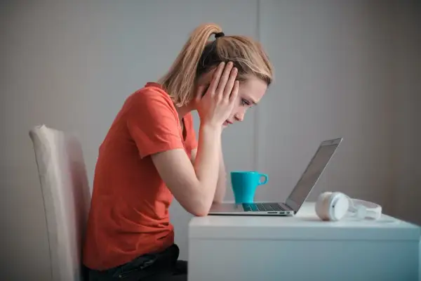 Zmartwiona dziewczyna z rękami na skroniach patrzy na laptopa. Może to być związane z zawieszeniem w prawach ucznia.