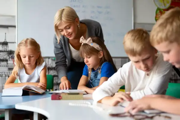Nauczycielka, jak dobra oligofrenopedagog, wspiera dzieci w nauce przy stolikach.