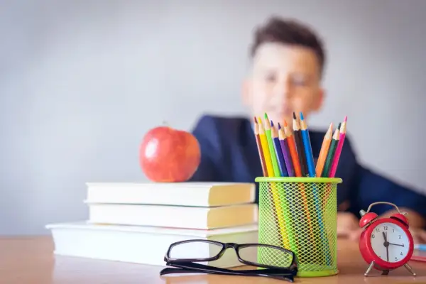 Chłopiec z fobią szkolną patrzy na stos książek, jabłko i kolorowe kredki. Zegar tyka, odmierzając czas do lekcji.