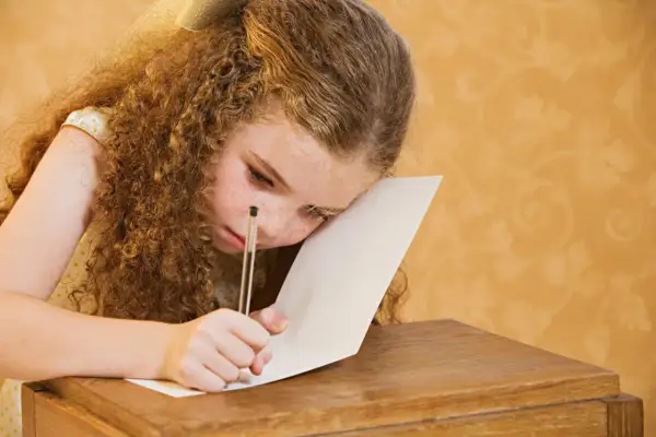 Dziewczynka z kręconymi włosami i piegami z trudem pisze, walcząc z dysleksją rozwojową.