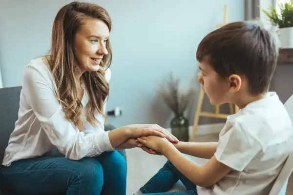 Kobieta wspiera chłopca, trzymając go za ręce. Rozmowa o wydłużeniu etapu edukacyjnego, budowanie pewności siebie.